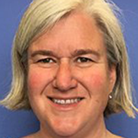 Headshot of a smiling woman with short light-blond hair, wearing a blue top against a plain blue background.