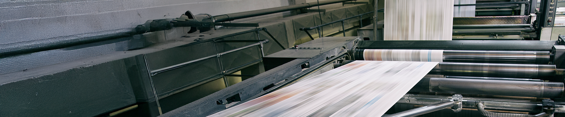 High-speed commercial printing press in motion, with blurred sheets of printed material feeding through large metal rollers.