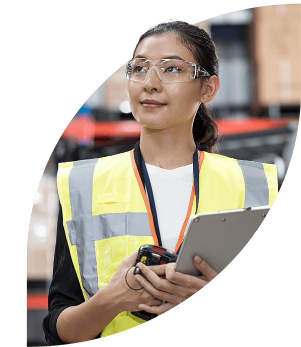 Woman wearing personal protective equipment and holding a clipboard stands in a warehouse