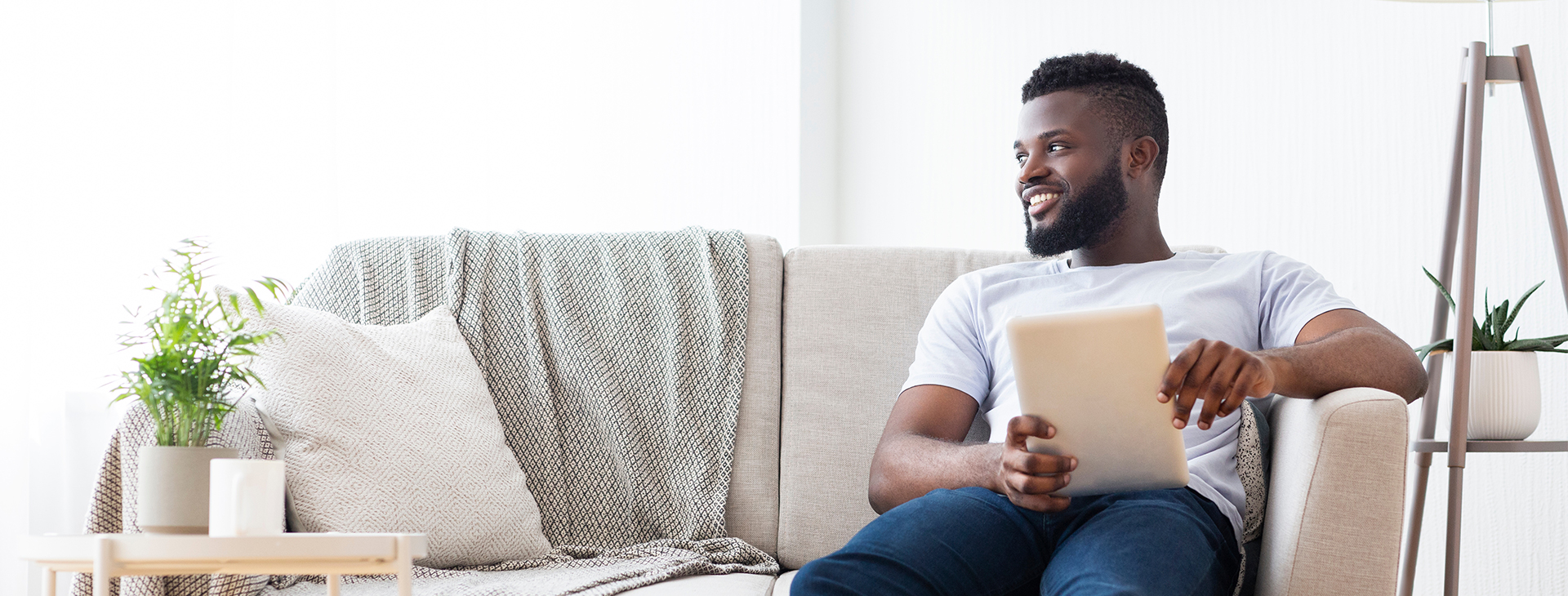 A man sits on his couch, reading his tablet and smiles