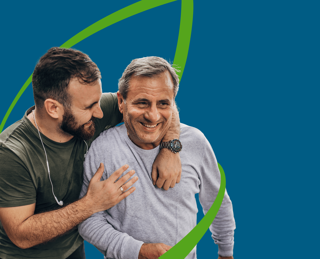 Man with earphones around his neck has his arm around the shoulder of his senior father, both smiling and laughing, with a green line forming the shape of a leaf around them.